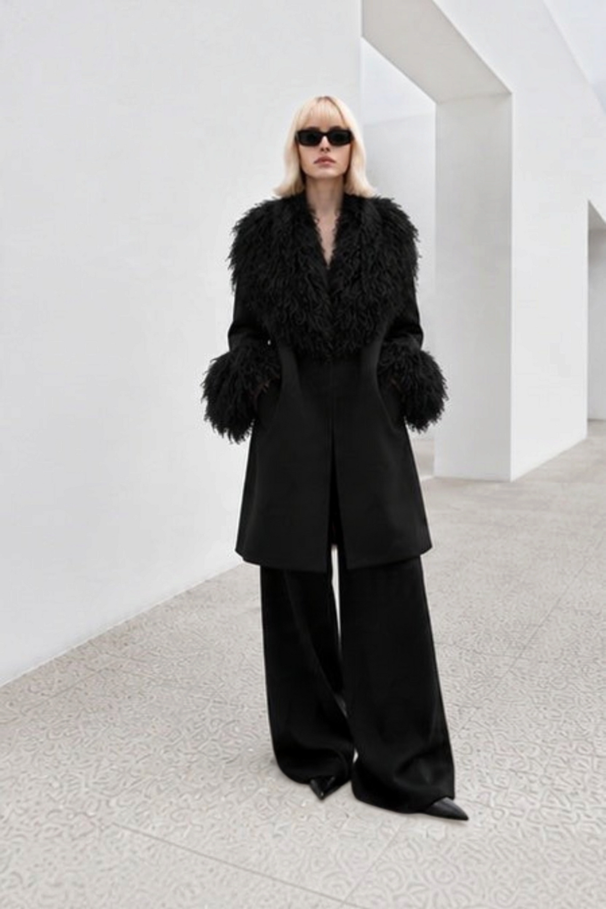 Model wearing Svart Studio black longline coat with detachable Mongolian sheep wool collar and oversized cuffs